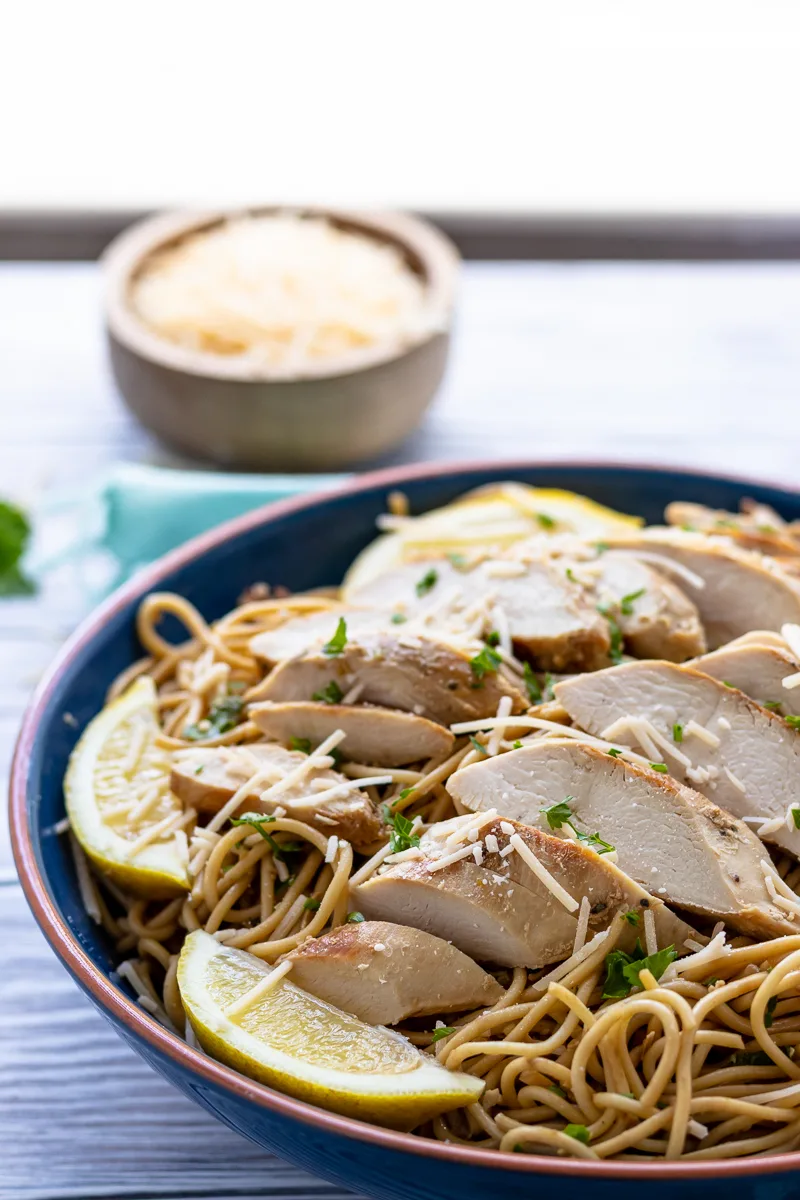 lemon chicken pasta ready to be served family style in a blue bowl set on a table near a window