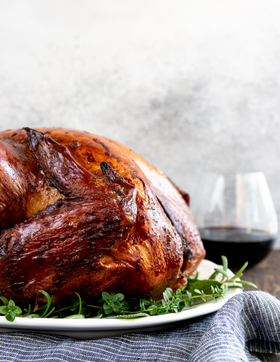 juicy smoked thanksgiving turkey ready to serve on a white platter with a glass of wine in the background