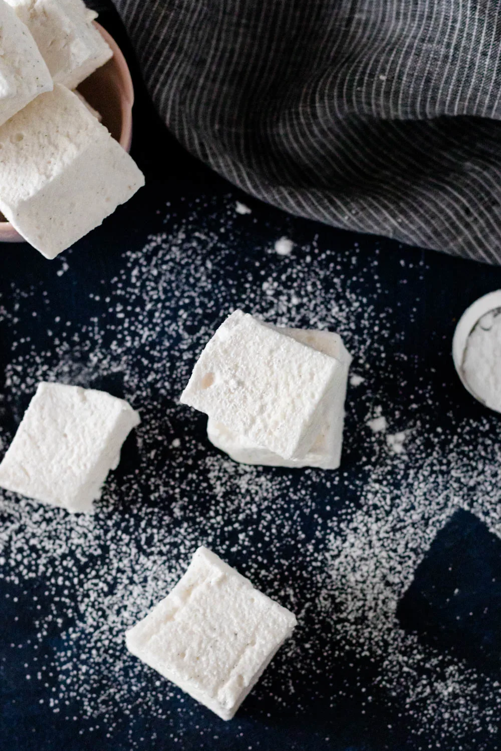 overhead image of cut and dusted marshmallows on a dark surface with a dark pinstripe napkin adding an accent in the top right of the frame