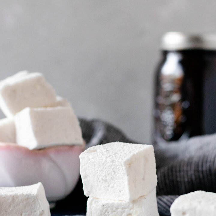 Homemade vanilla marshmallows in a bowl and stacked on a textured kitchen surface