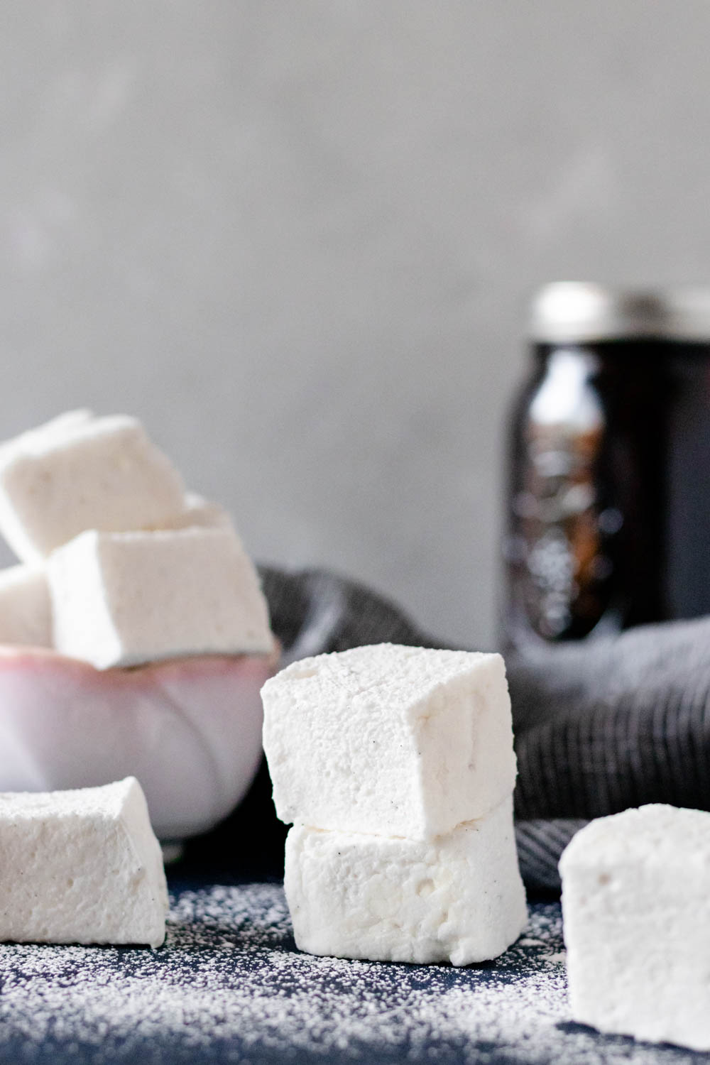 Homemade vanilla marshmallows in a bowl and stacked on a textured kitchen surface 