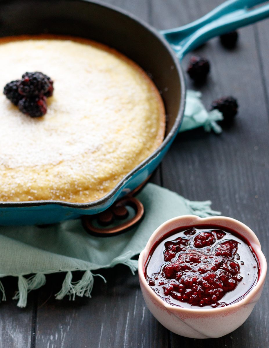 angled picture of the cast iron skillet pancake with the berry compote in a small bowl up front