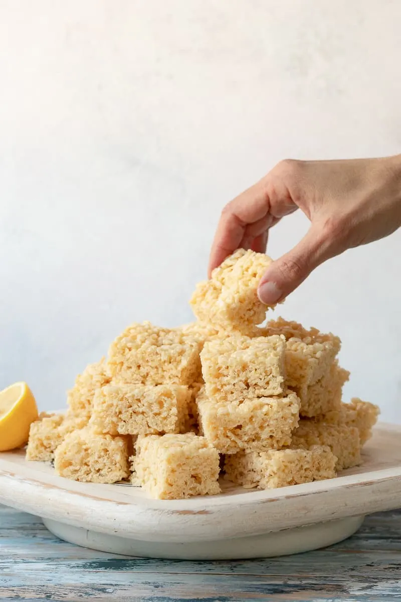 hand reaching to grab the top lemon cereal treat off the stack on the platter