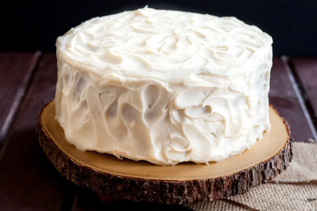 horizontal image of a red velvet cake with cream cheese frosting, unsliced, on a wooden cake board