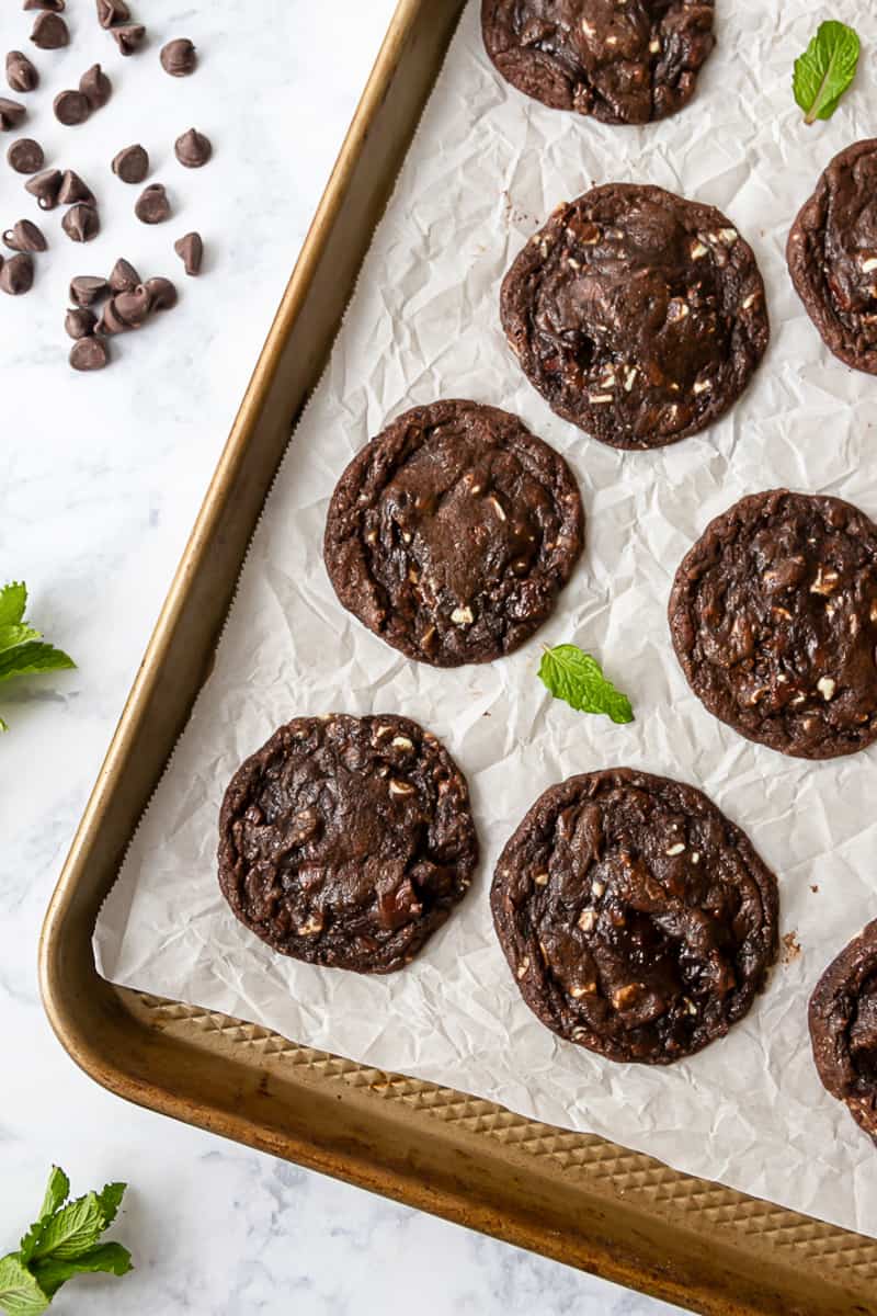 top view of the chocolate mint cookies on a baking sheet with scattered fresh mint leaves