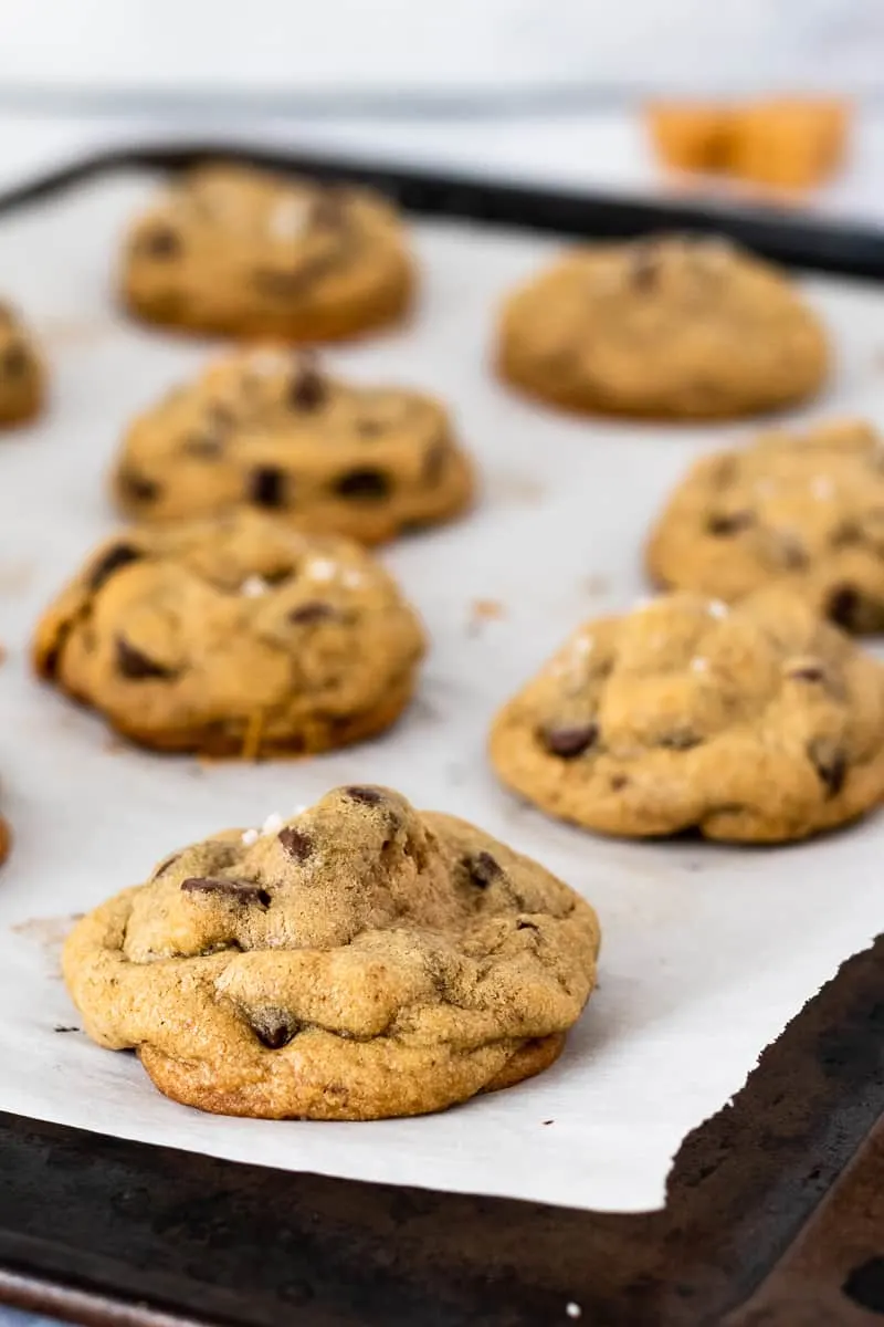 caramel stuffed chocolate chip cookies resting on a baking sheet lined with parchment