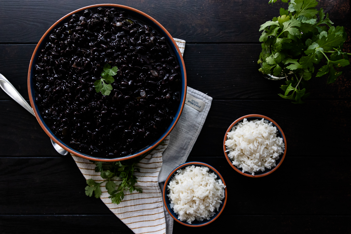 overhead shot of black beans in a serving bowl with two smaller bowls of white rice on the side