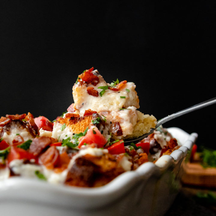 kentucky hot brown casserole ready to serve. A portion is balanced on a large serving spoon suspended above the casserole
