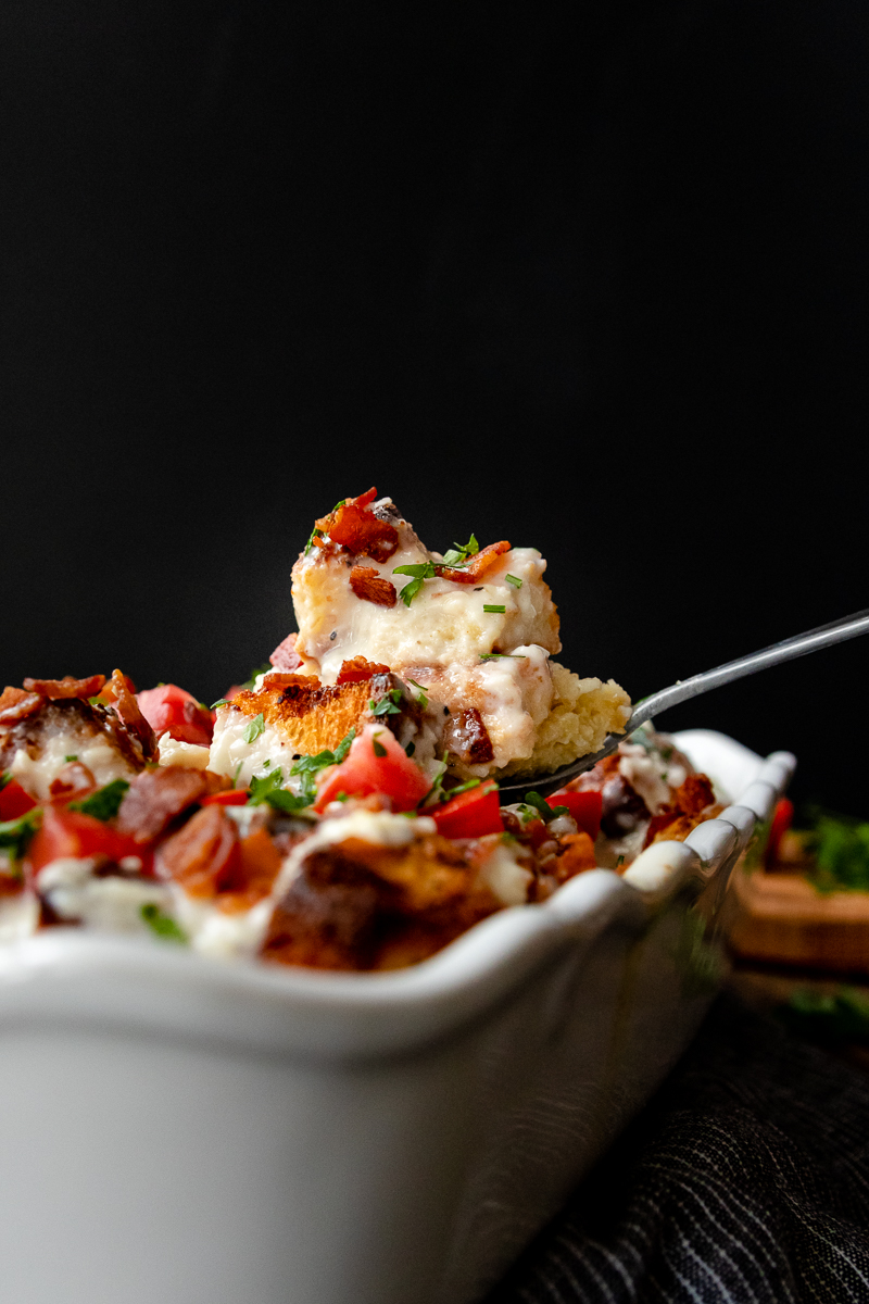 kentucky hot brown casserole ready to serve. A portion is balanced on a large serving spoon suspended above the casserole 
