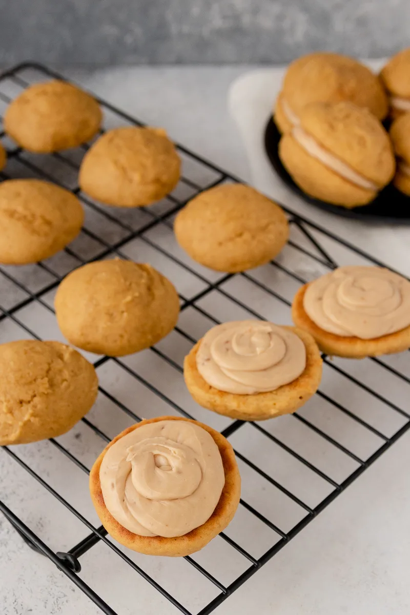 pumpkin whoopie pies half filled on a cooling rack to show approximately how much frosting I used per cookie sandwich