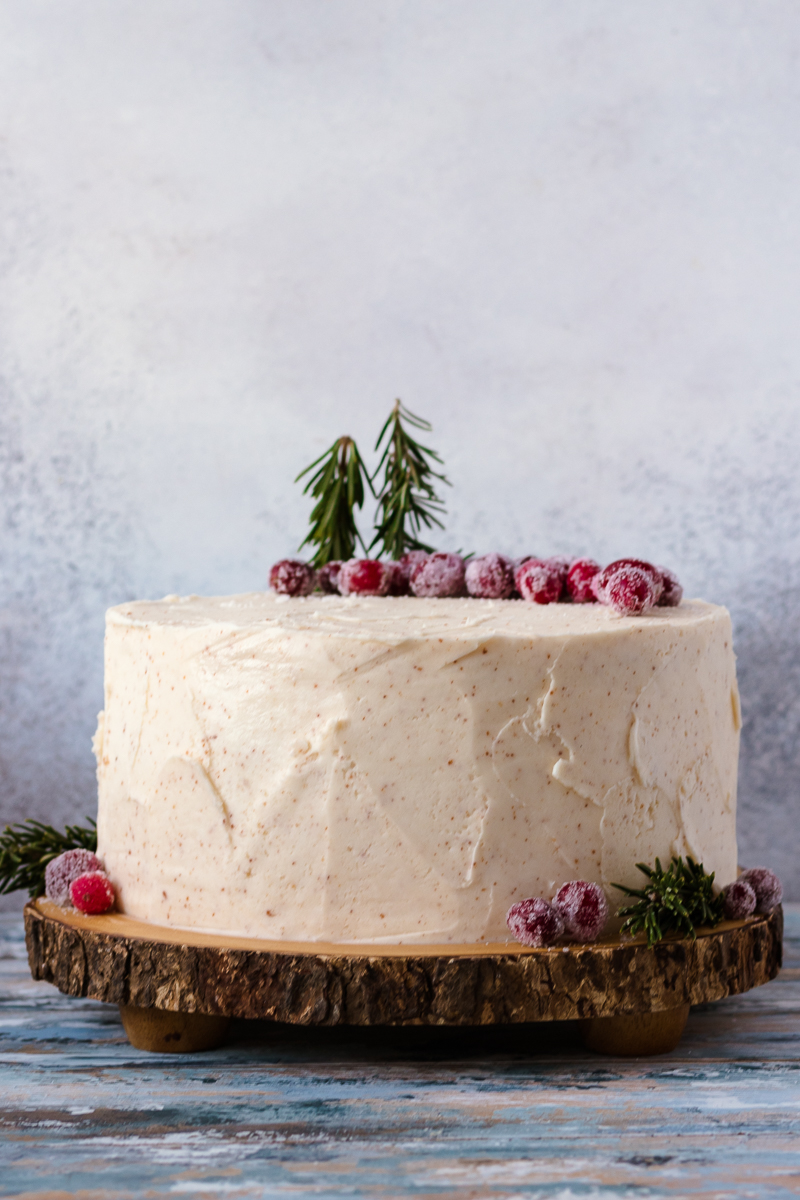 eggnog cake on a wooden cake plate with a mottled grey background