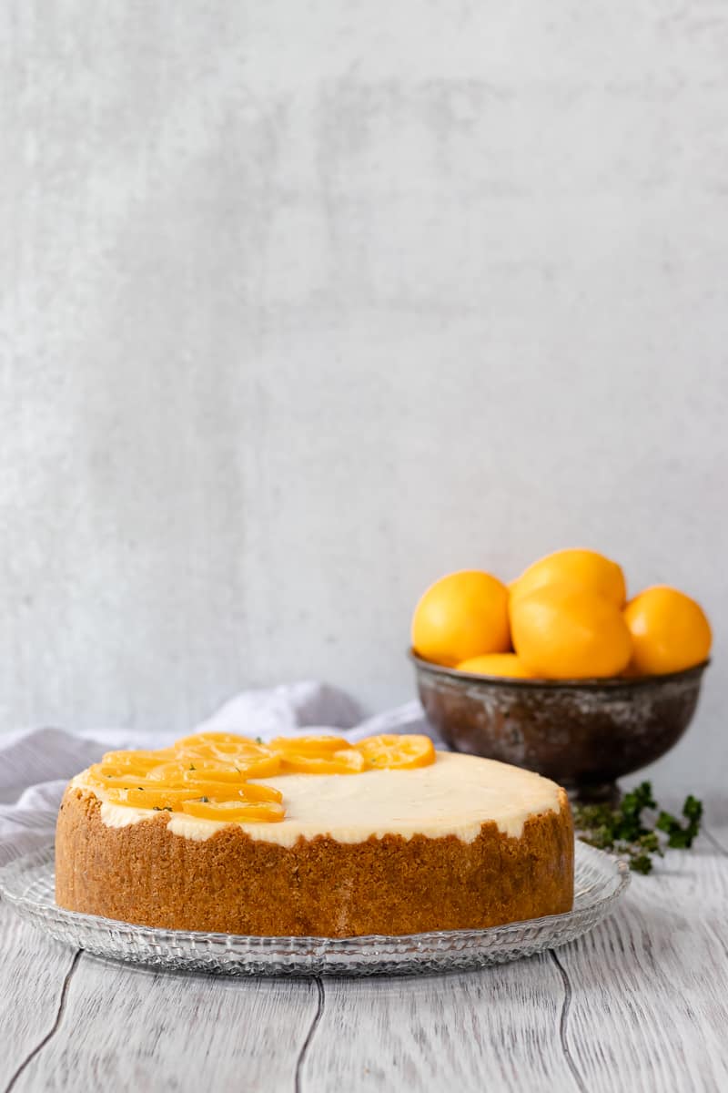 meyer lemon cheesecake on a glass plate with a bowl of meyer lemons in the background