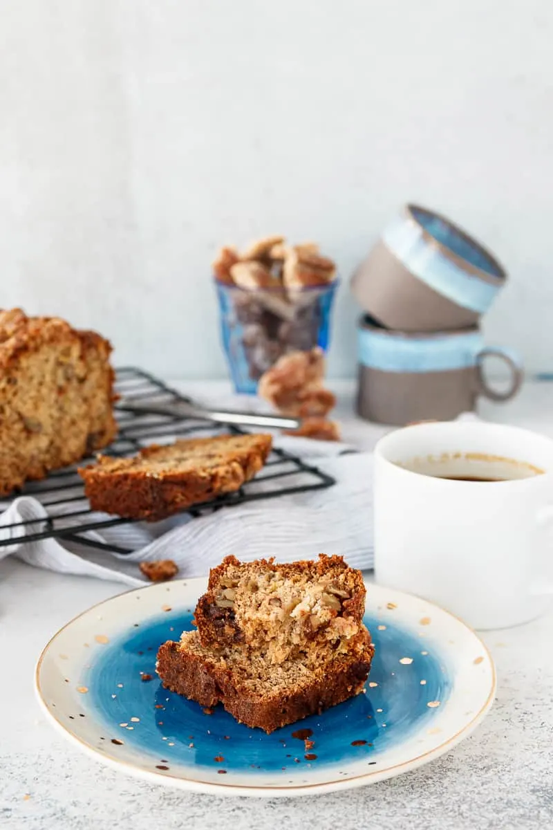 slice of praline banana bread stacked on a serving plate near coffee cups. A serving suggestion