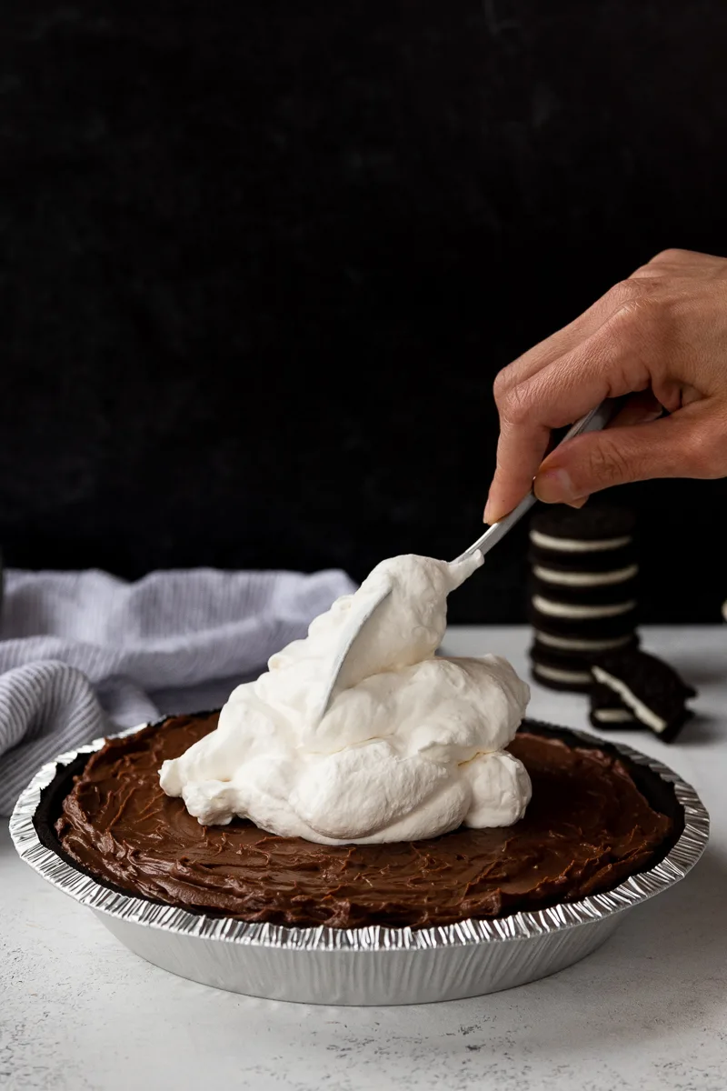 adding whipped cream to the chocolate pudding pie