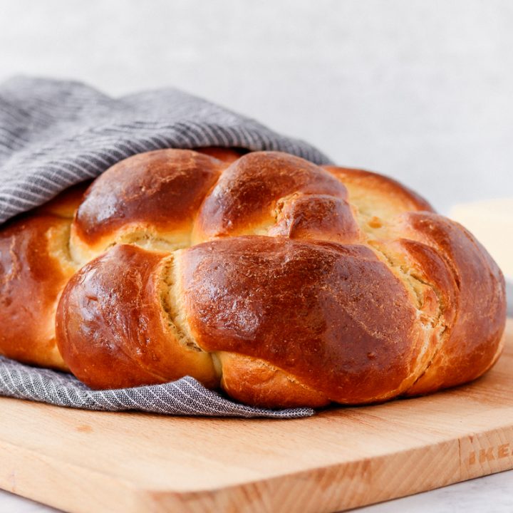 baked challah bread wrapped in a tea towel sitting on a cutting board