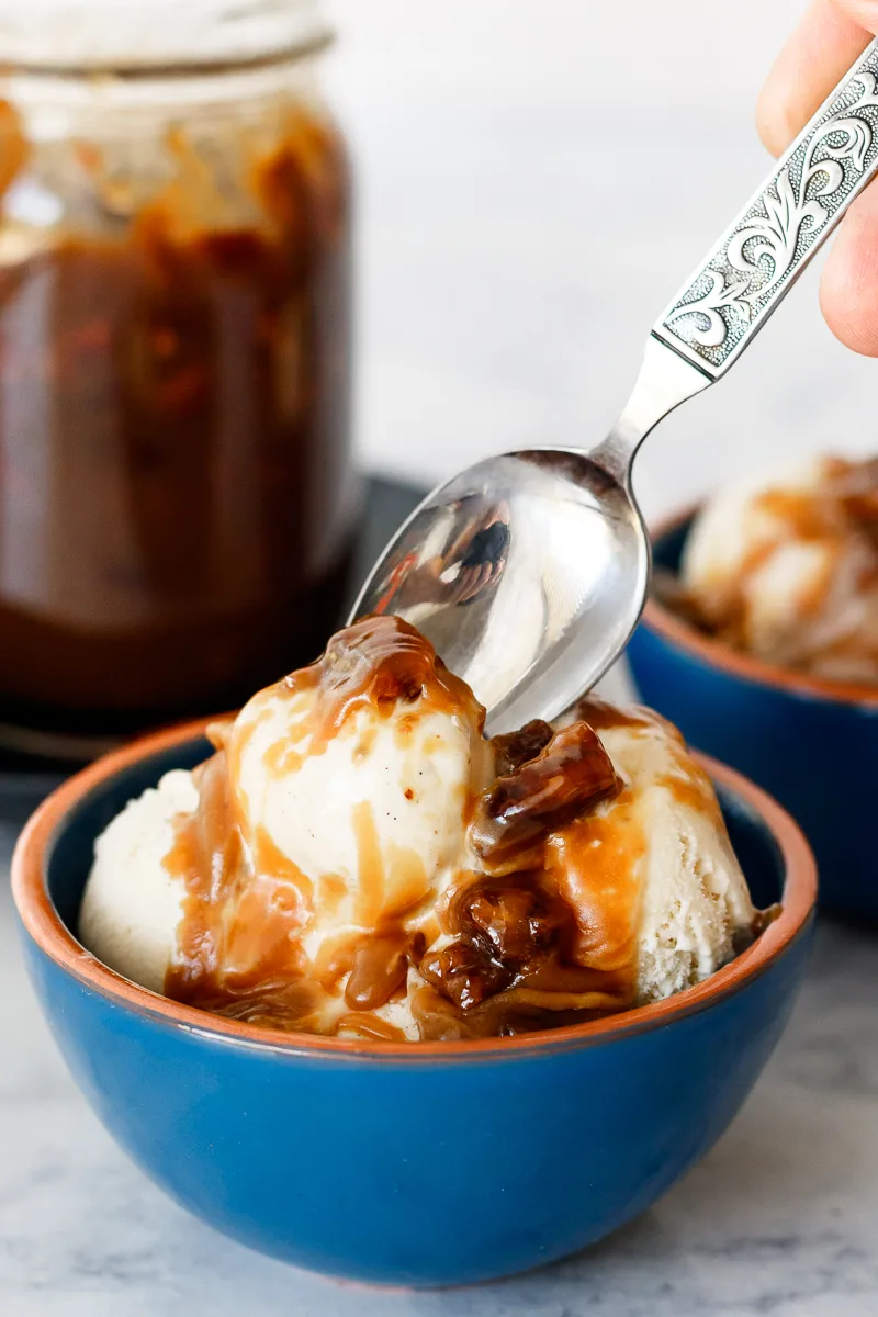 spoon digging into a bowl of ice cream with pecan praline sauce