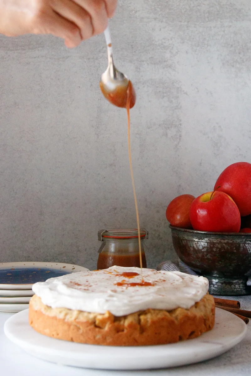spoon drizzling caramel on a frosted apple breakfast cake