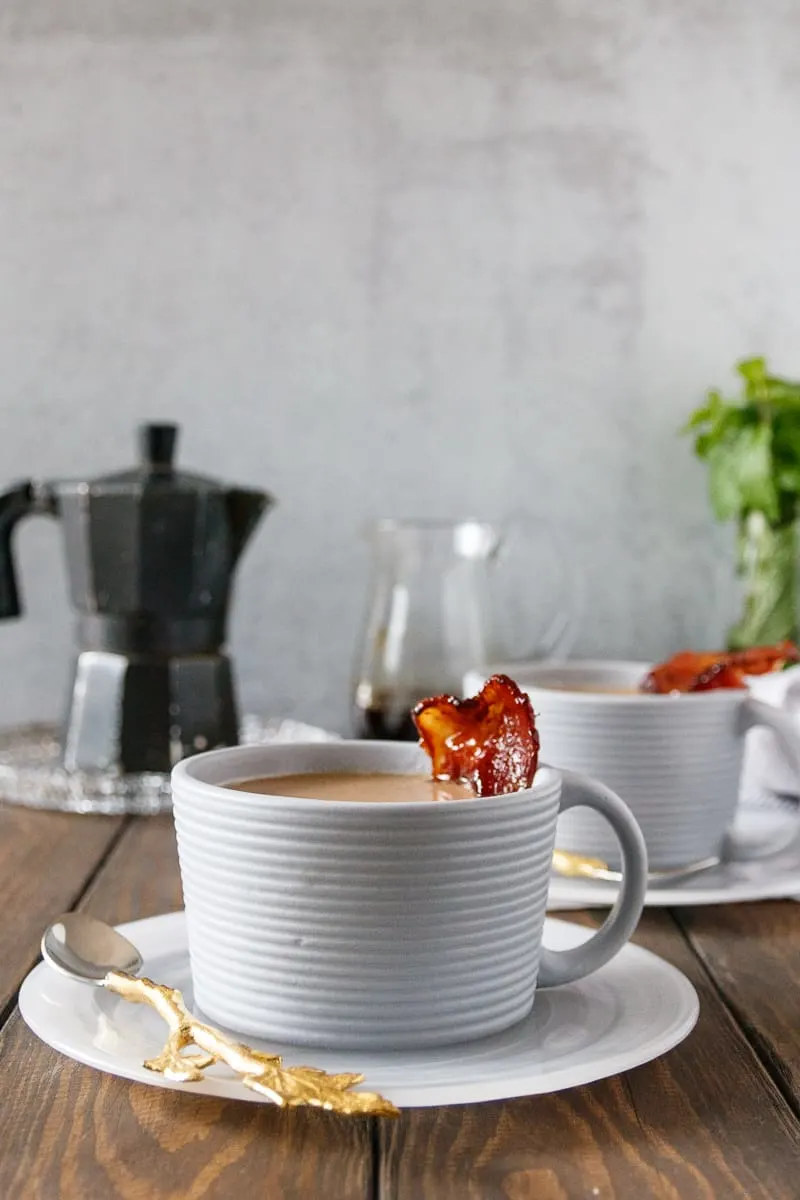 maple bacon latte in a grey textured mug with a slice of maple candied bacon as garnish