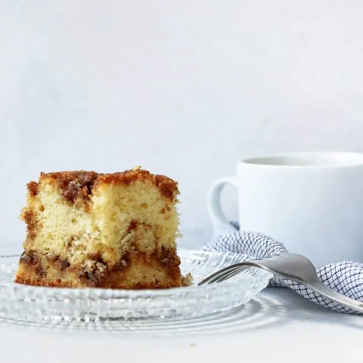 slice of easy sour cream coffee cake on a glass plate with a white mug of coffee in the background