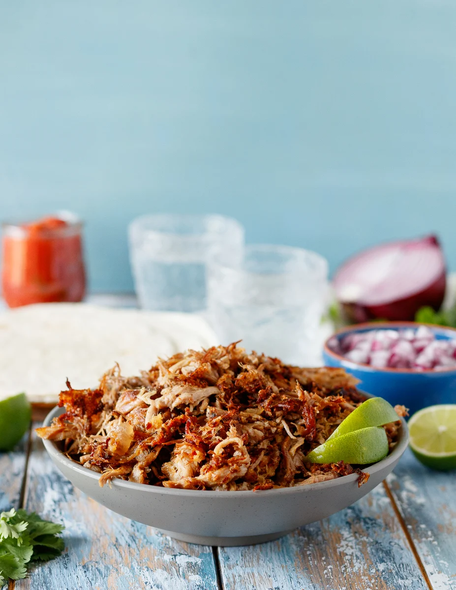 Easy slow cooker carnitas in a grey bowl with lime wedges for serving