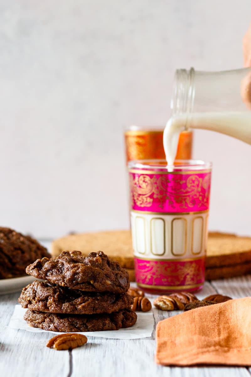 milk pouring in the background with a stack of double chocolate pecan toffee cookies in the foreground
