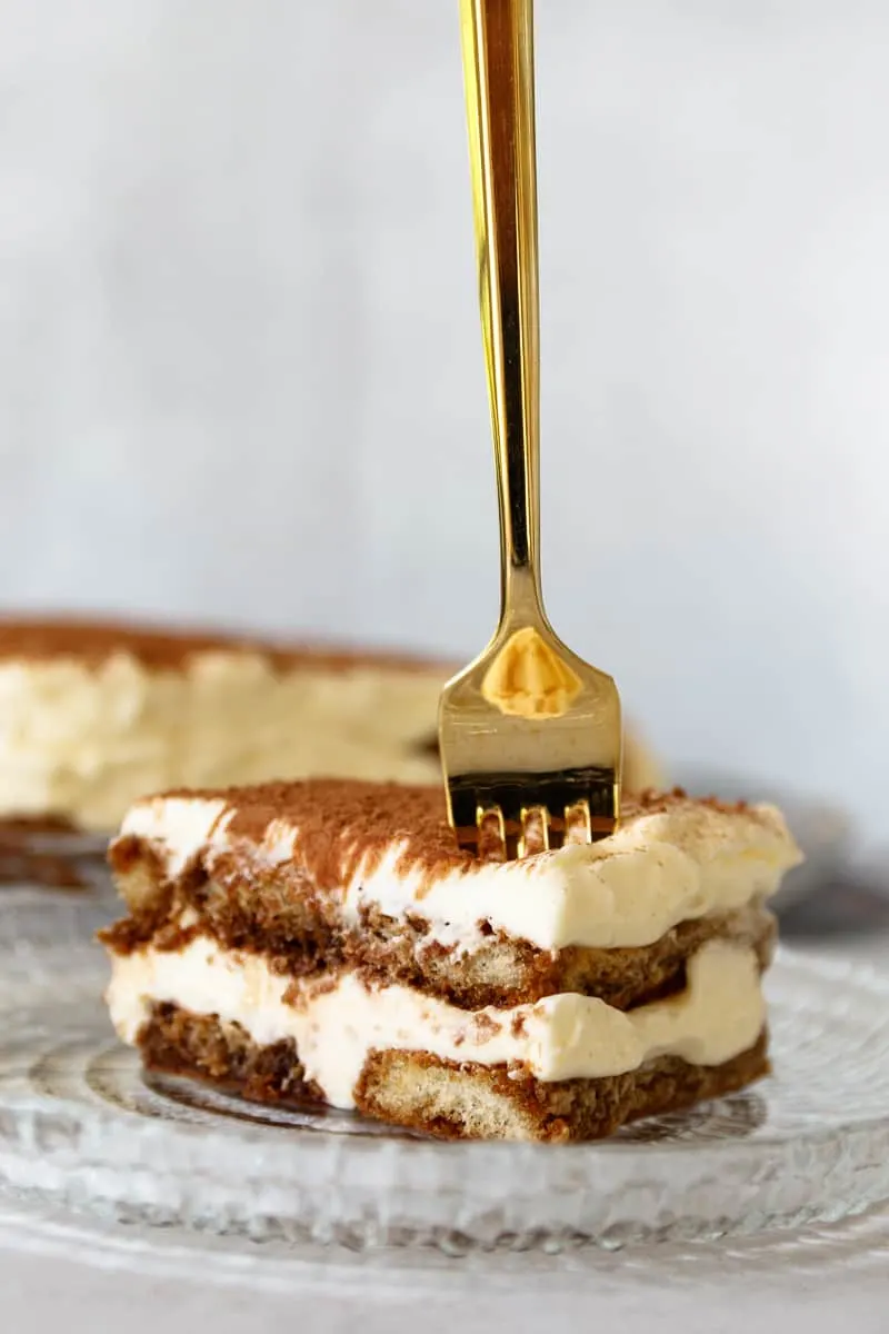 golden fork vertically positioned in a slice of tiramisu, poised to break off a piece