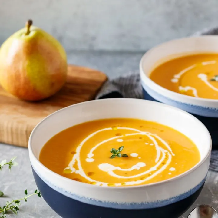 pear and sweet potato soup in blue and white bowls with a drizzle of heavy cream to add fancy detailing