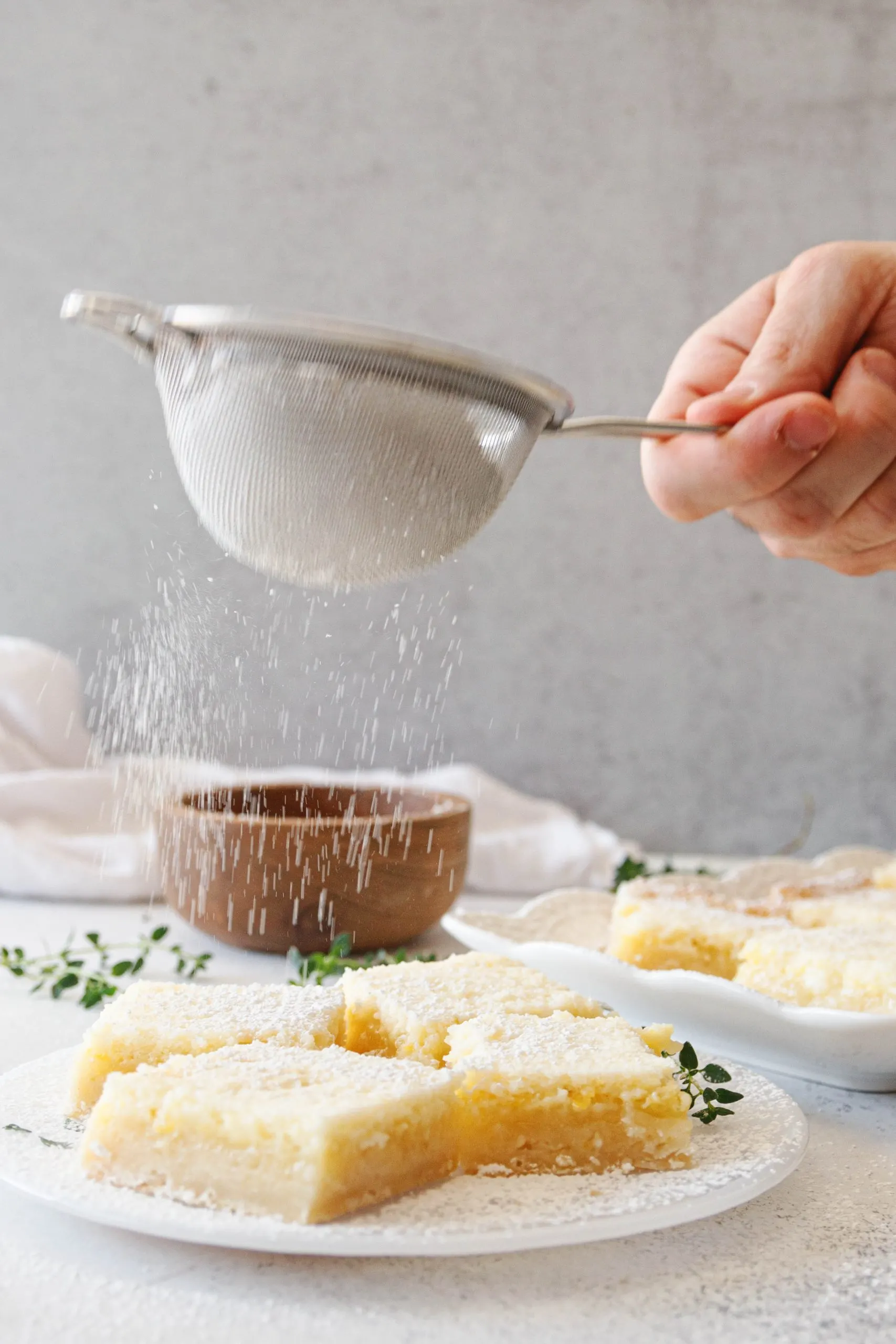 The Godfather's hand shaking a fine mesh sieve with powdered sugar over a plate of lime bars