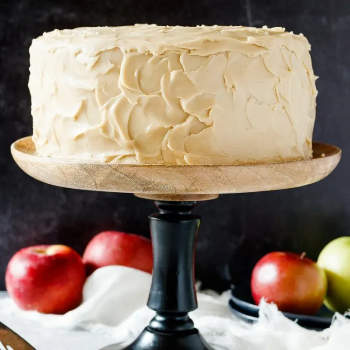 caramel apple spice cake on a black and wooden cake stand with apples in the background