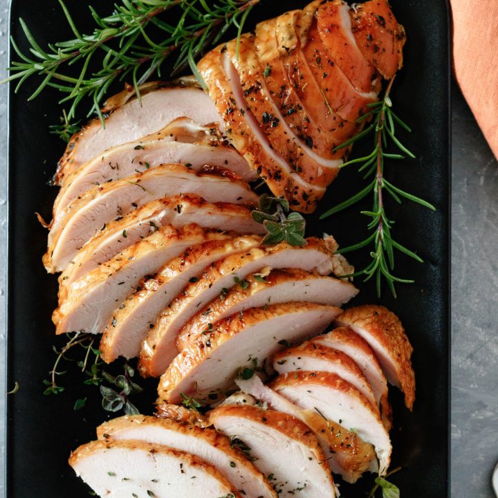 top view of a sliced and plated pellet grill smoked turkey breast on a black plate with fresh herb garnish