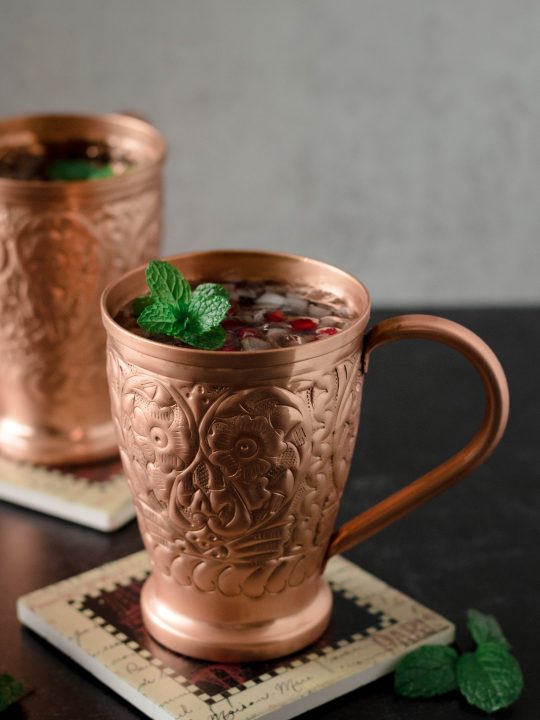 angled picture of pomegranate moscow mules garnished with mint in copper mugs