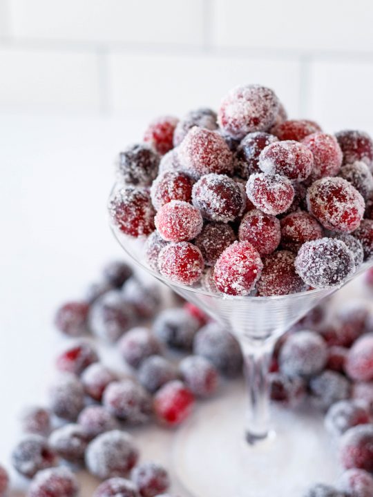 angled view of sugared cranberries piled in a martini glass with a white tile background