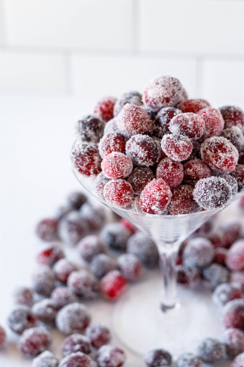 angled view of sugared cranberries piled in a martini glass with a white tile background