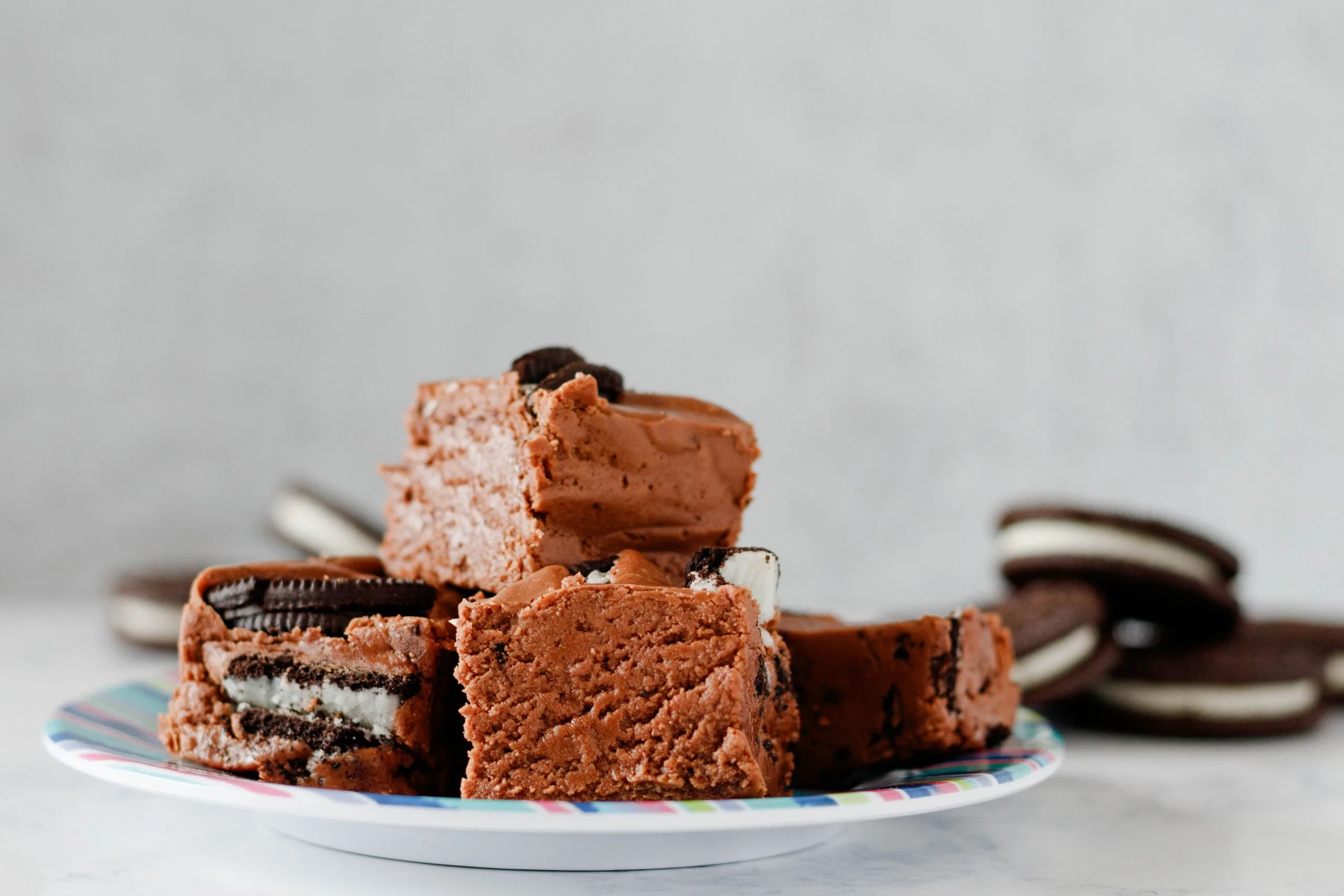 horizontal photo of the double chocolate oreo fudge on a striped plate. Cubes are arranged on a small plate to show texture of squares with cookies on the cut side and without