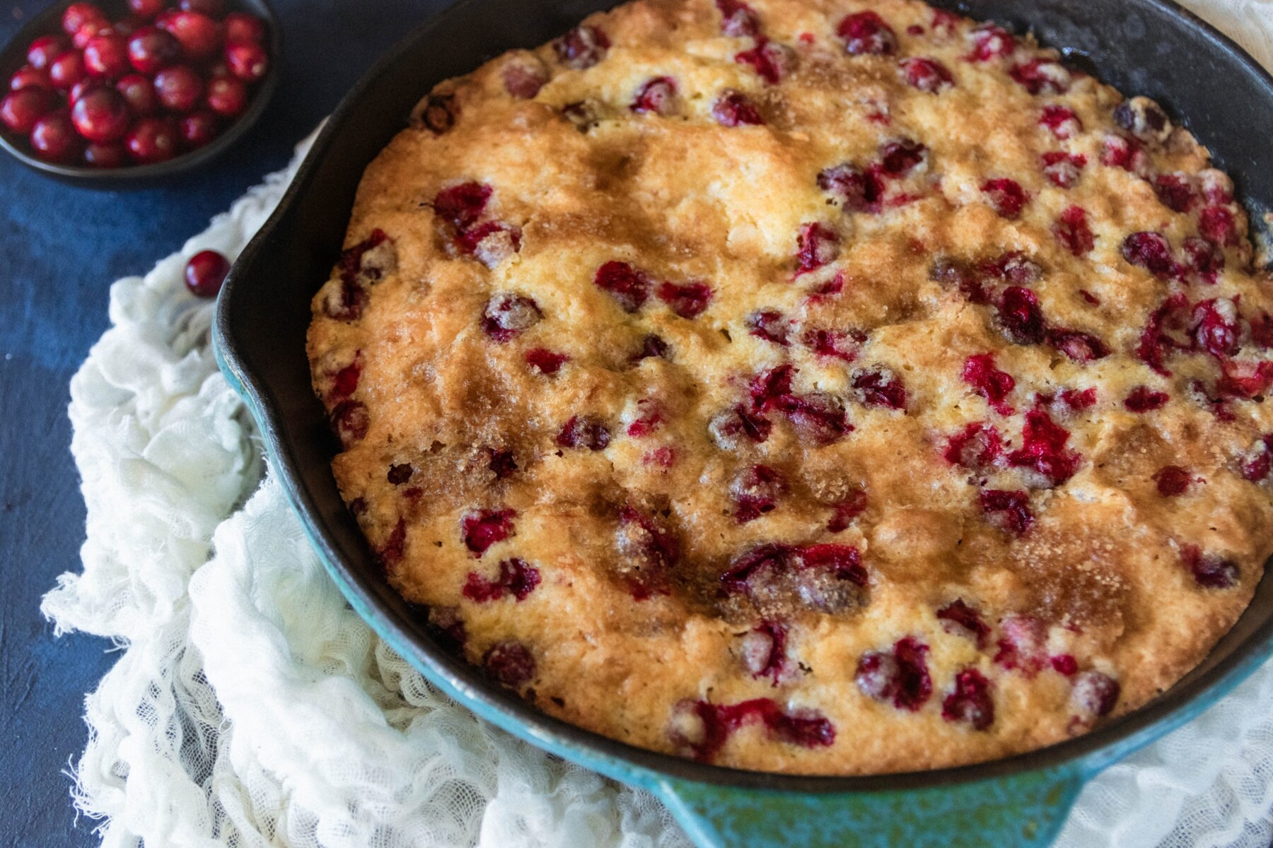 angled picture of the fresh cranberry skillet cake in a blue enameled cast iron skillet sitting on a napkin