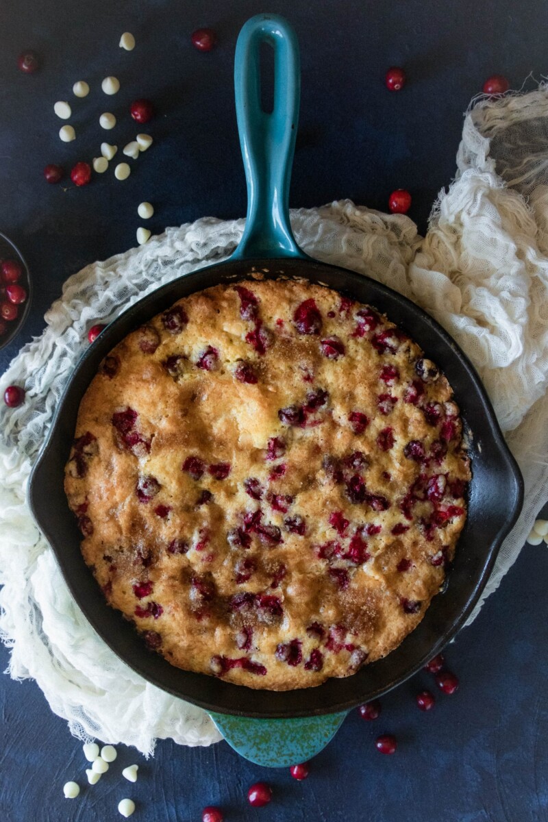 top view of the cake in the skillet with scattered cranberries and white chocolate chips