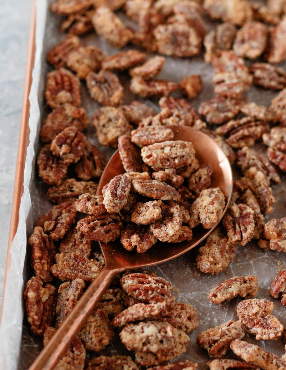 whiskey candied pecans on a sheet pan, scooped by a copper spoon
