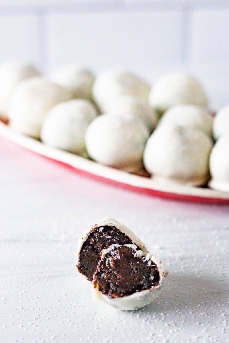 Cut sparkling chocolate cookie truffle on a white surface in front of a tray of more cookie truffles