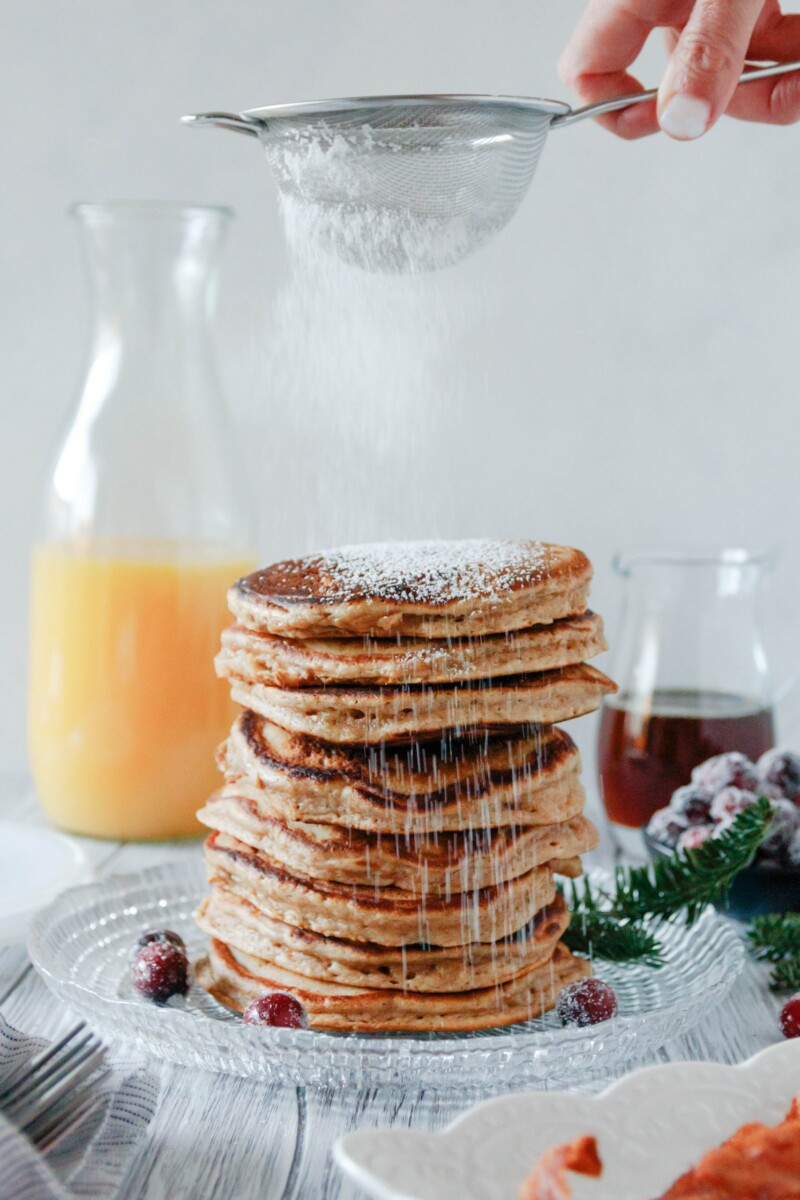 small sieve with powdered sugar dusting a big stack of pancakes ready to serve!