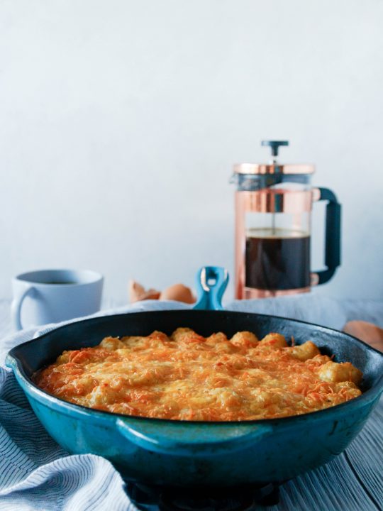 tater tot breakfast casserole made in a blue case iron skillet with a french press in the background