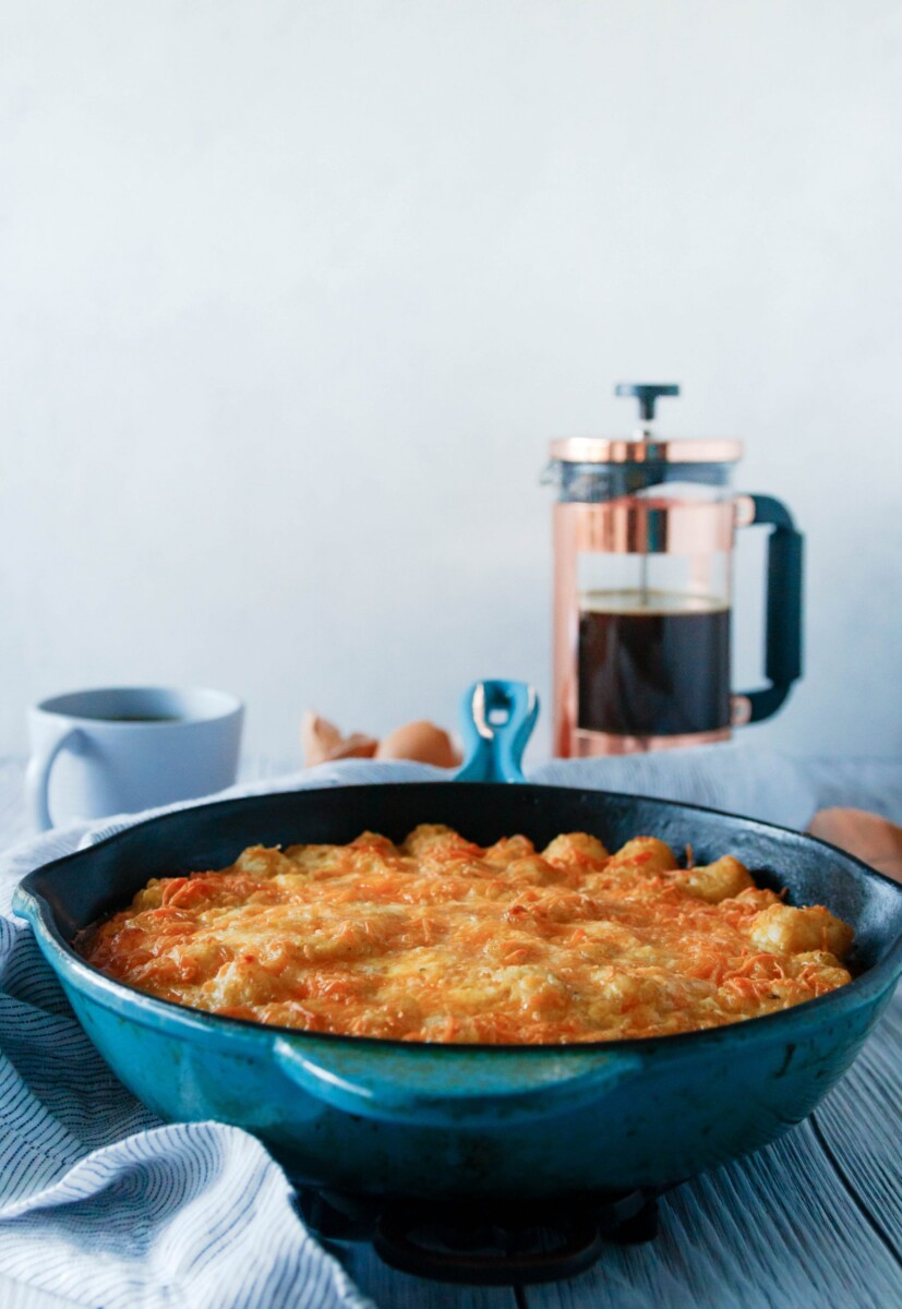 tater tot breakfast casserole made in a blue case iron skillet with a french press in the background