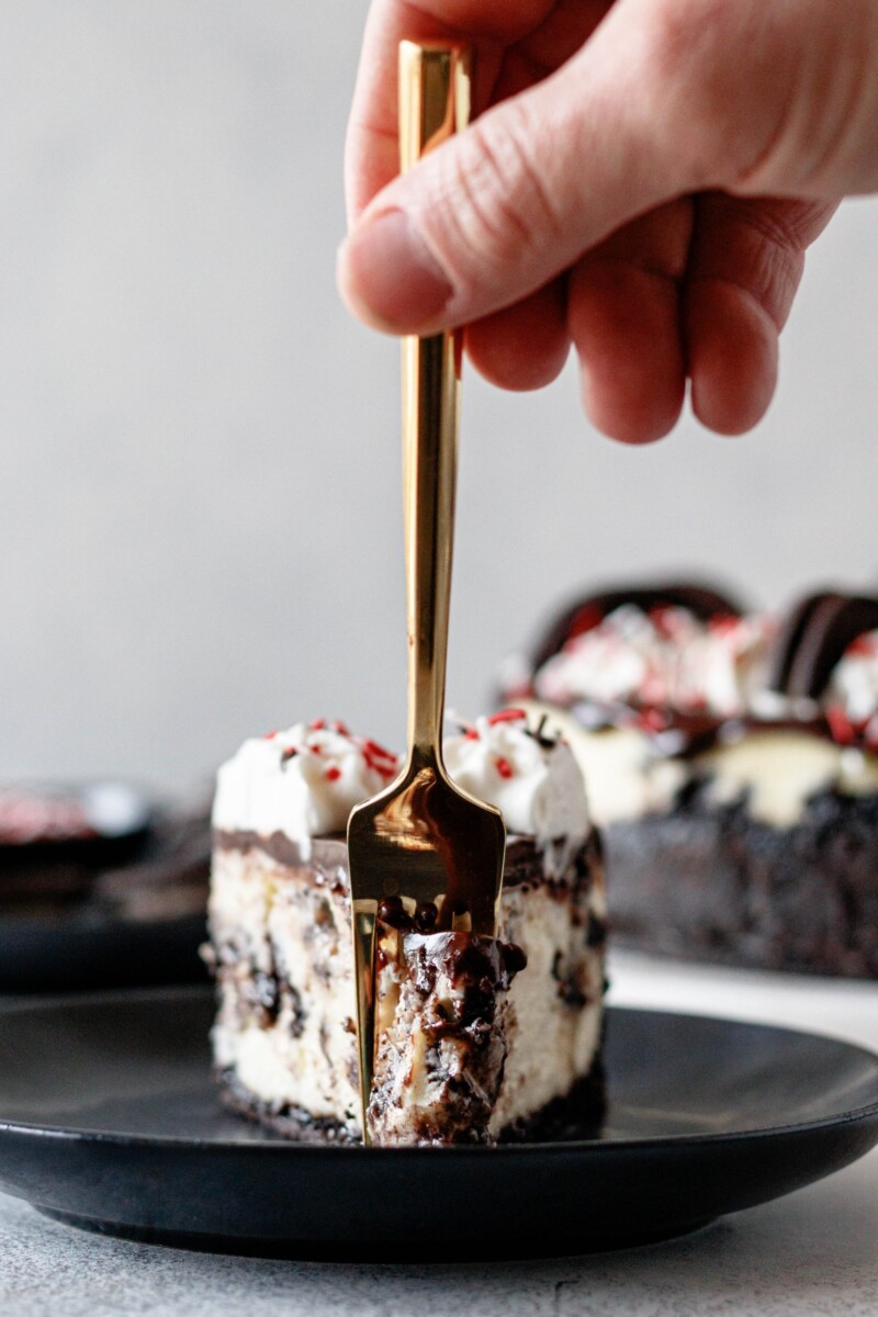 gold fork cutting into a slice of peppermint bark cheesecake