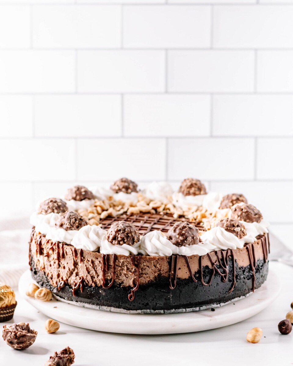 whole chocolate hazelnut cheesecake on a white marble plate, fully garnished and ready to slice