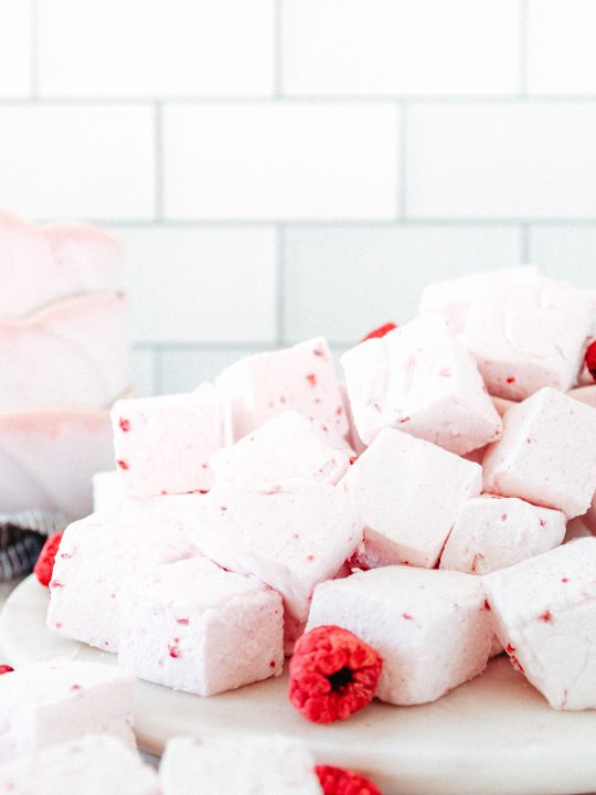 close up of a pile of pink raspberry marshmallows on a marble plate accented with freeze-dried raspberries