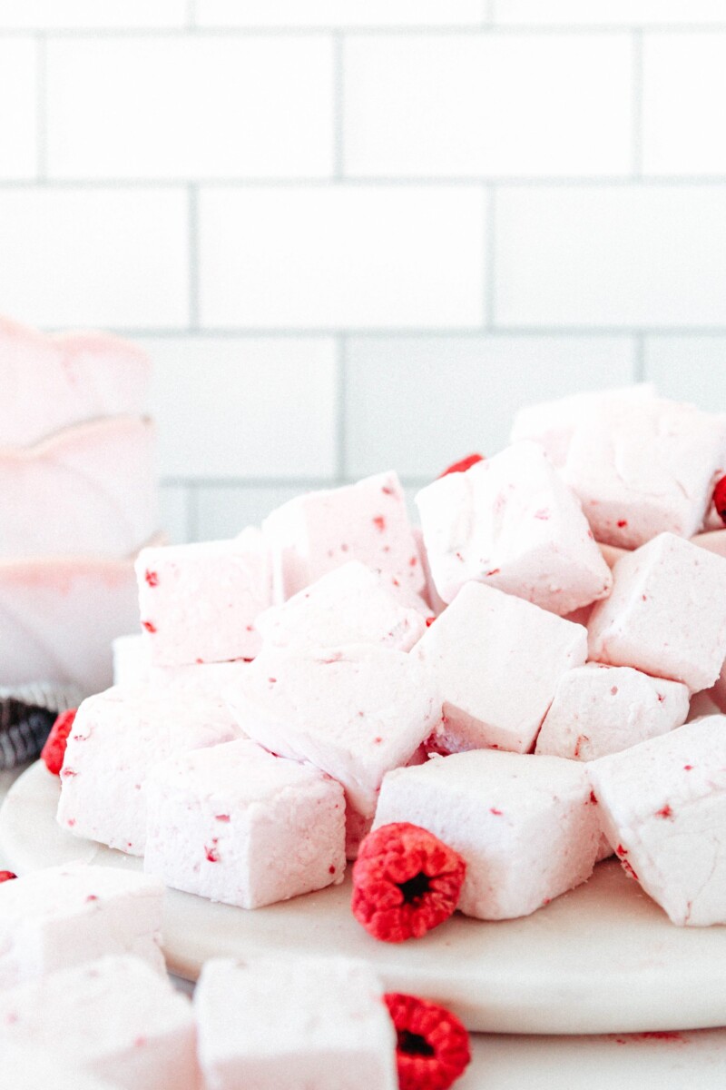 close up of a pile of pink raspberry marshmallows on a marble plate accented with freeze-dried raspberries