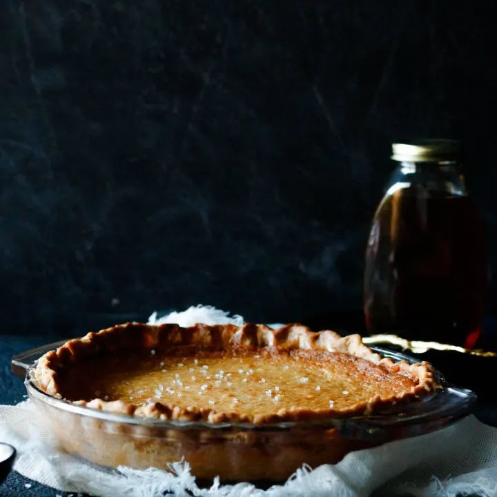 whole salted whiskey honey pie sitting on a fringed napkin. The background is black and you can see a partial outline of a jar of honey