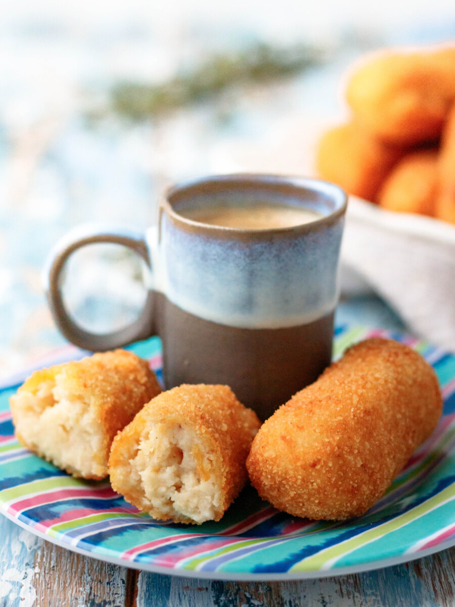 angled view of two croquetas de pollo on a colorful saucer with a small cup of cuban coffee