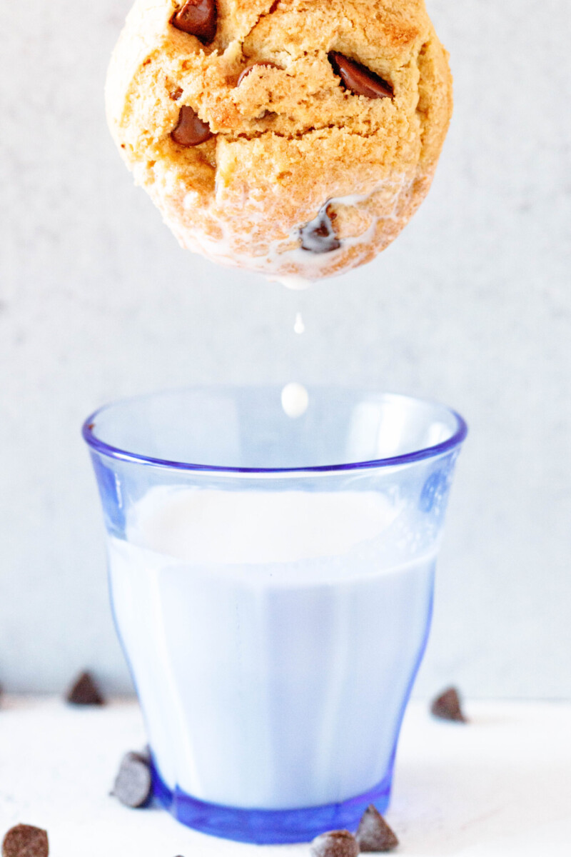 chocolate chip cookie dunked into a glass of milk with a few drops of milk falling back into the glass