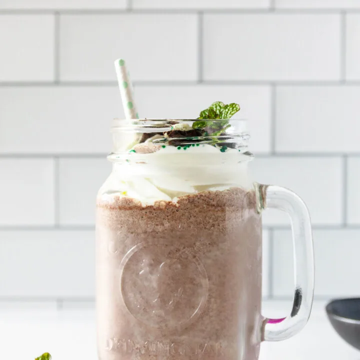 one creamy mint oreo milkshake sitting on a colorful coaster on a white counter with a white subway tile background