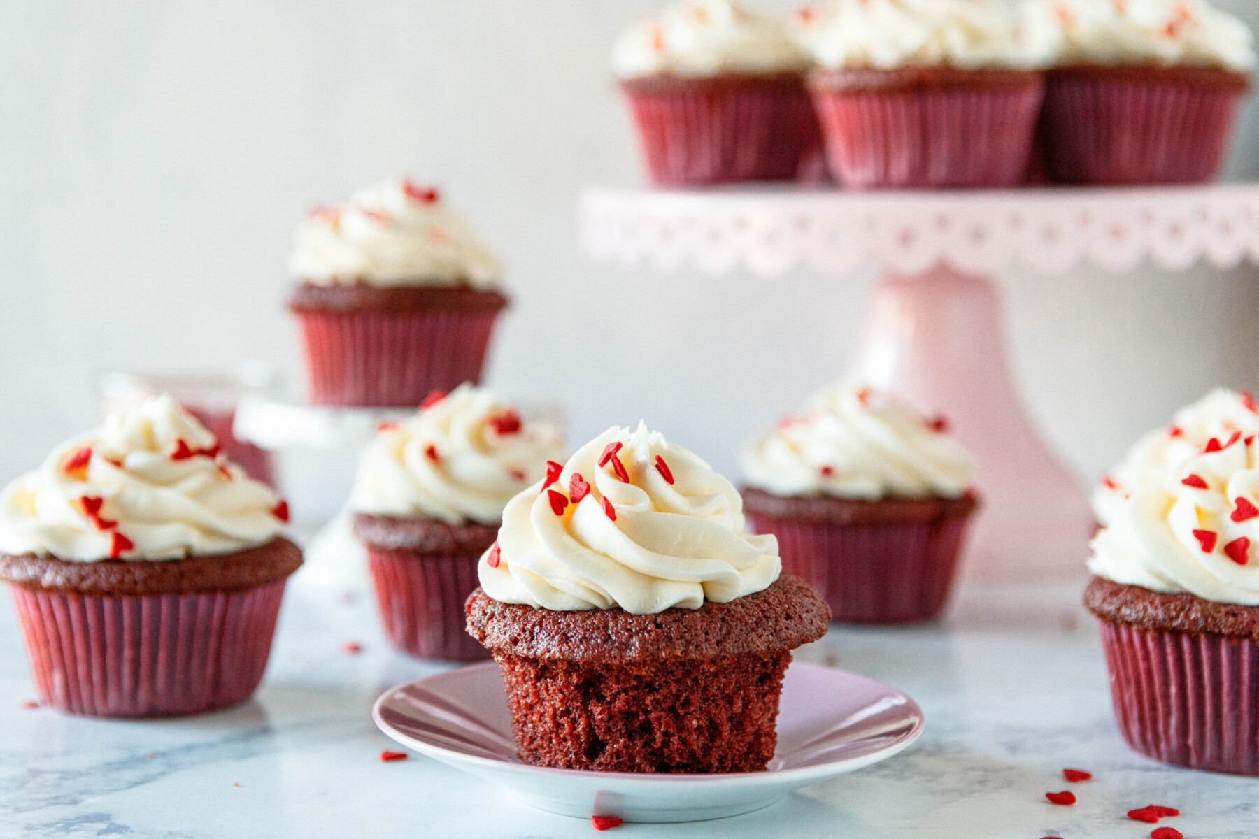 horizontal picture of the red velvet cupcakes with one of them removed from the paper liner and sitting on a mauve pink plate